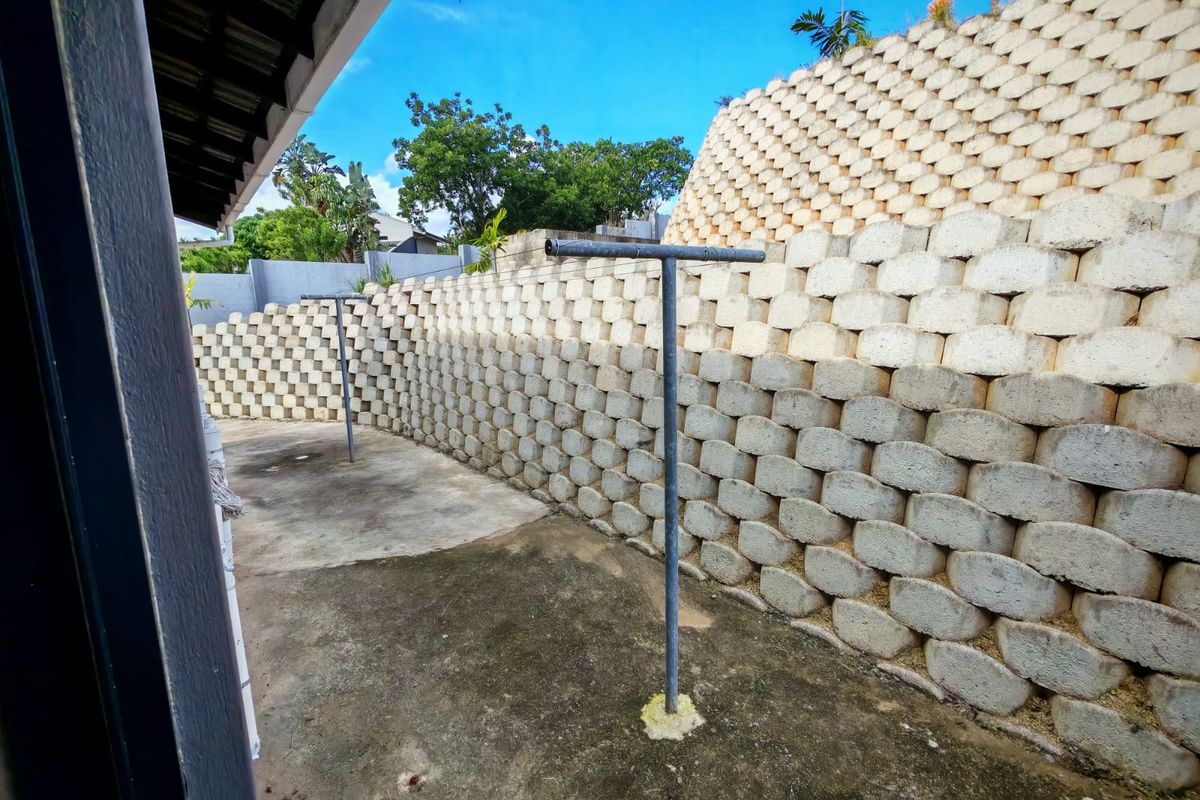A rear outdoor utility area featuring concrete paving and a large tiered retaining wall structure with fixed metal washing lines.