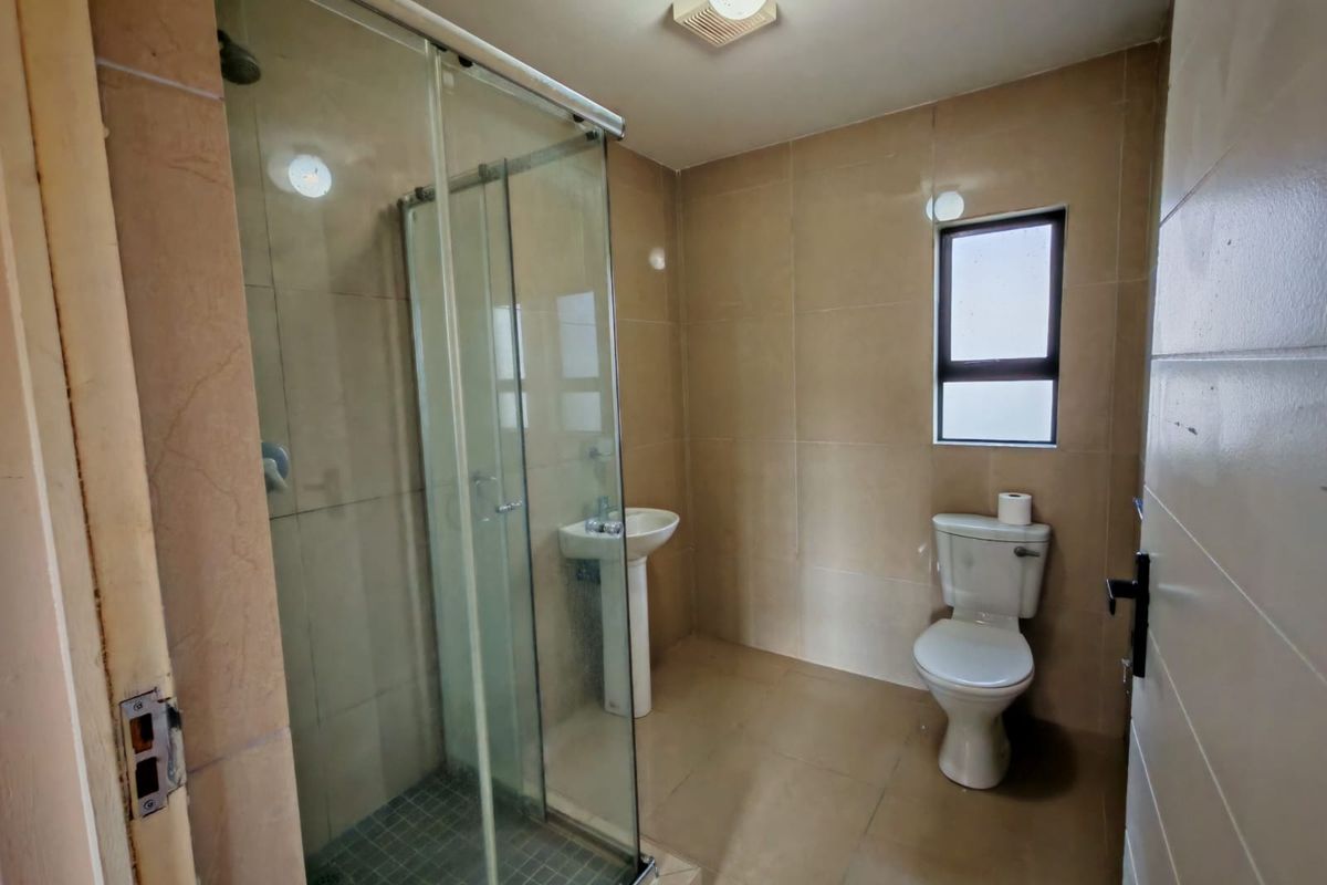 A functional bathroom featuring a glass-enclosed shower, pedestal basin, and toilet with neutral wall and floor tiling.