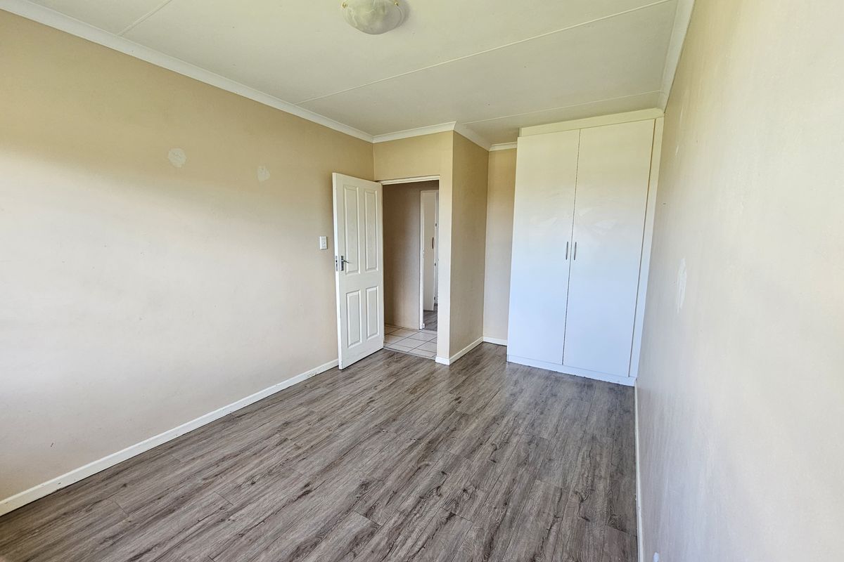 An empty bedroom featuring modern laminate flooring, a built-in wardrobe, and neutral wall finishes, providing a blank canvas for personalization.