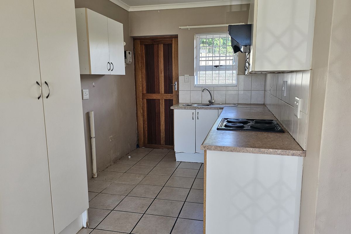 A functional kitchen featuring built-in cabinetry, laminate countertops, an electric hob, and tiled flooring, offering a blank canvas for potential modern updates.