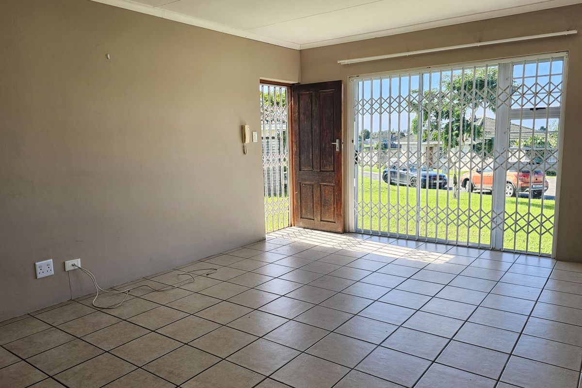 An empty living room featuring tiled flooring, a security gate, and a sliding door providing access to the exterior.