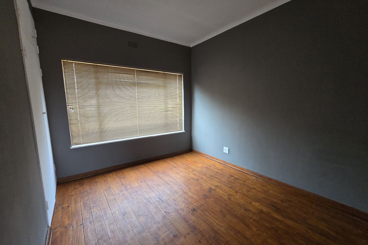 An empty bedroom featuring original timber flooring, dark grey walls, and fitted venetian blinds, offering a blank canvas for personalization.