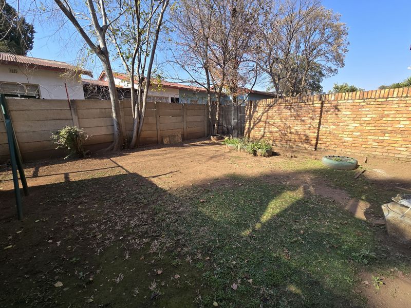 A private rear garden area featuring a mix of precast concrete and exposed brick boundary walls with security razor wire.