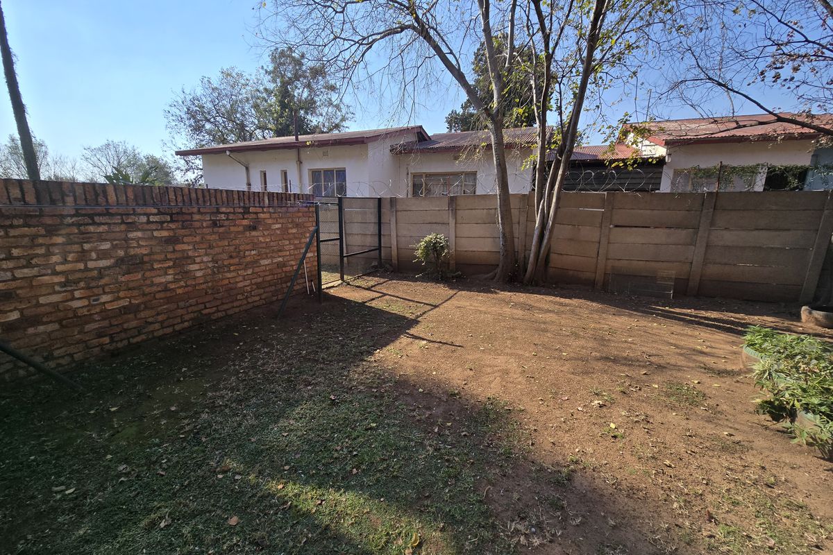 A rear garden area featuring a mix of brick and precast concrete boundary walls with security razor wire and mature trees.