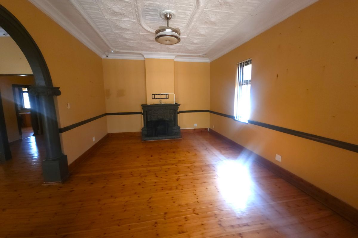 Spacious living room featuring original pressed metal ceilings, timber flooring, and a central fireplace, offering a character-filled blank canvas for renovation.