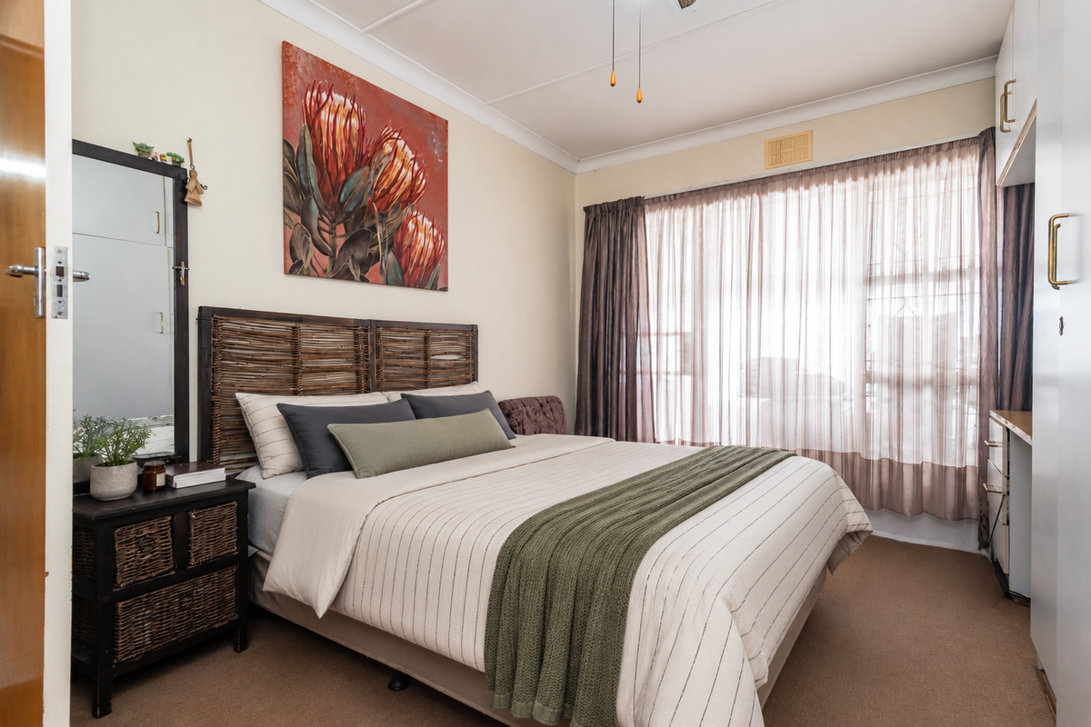 A well-lit bedroom featuring built-in cabinetry, carpeted flooring, and large windows with sheer curtains, providing a comfortable and functional living space.