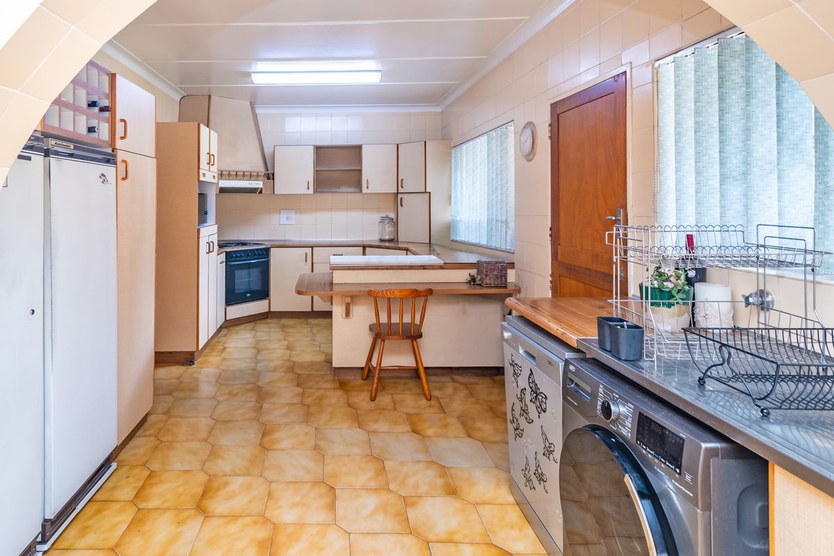A dated kitchen featuring original cabinetry, tiled flooring, built-in oven, and extractor fan, offering a functional layout with potential for modernization.