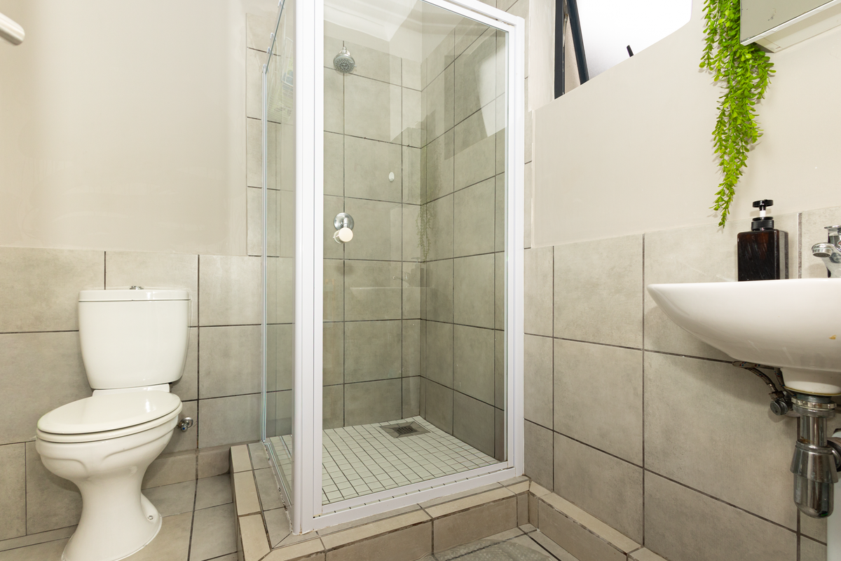 A compact bathroom featuring a tiled shower enclosure, a standard toilet, and a wall-mounted basin with exposed plumbing.