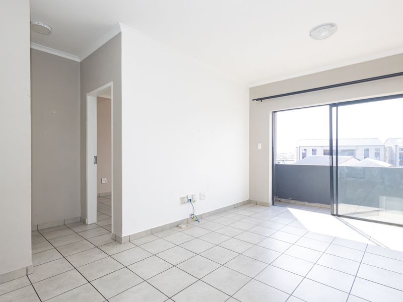 An empty, well-lit living area featuring neutral tiled flooring and a large sliding glass door providing access to an outdoor balcony.