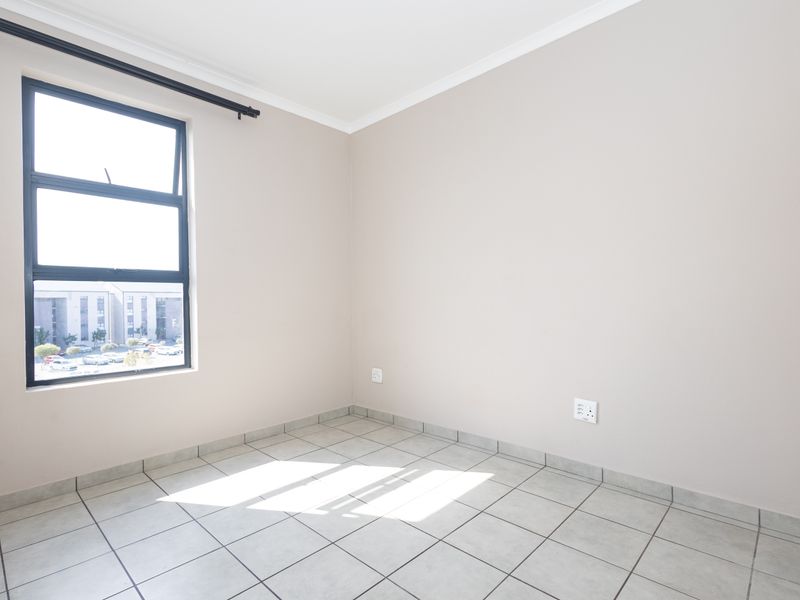 A bright, empty bedroom featuring neutral wall paint, tiled flooring, and a large aluminium-framed window with an installed curtain rail.
