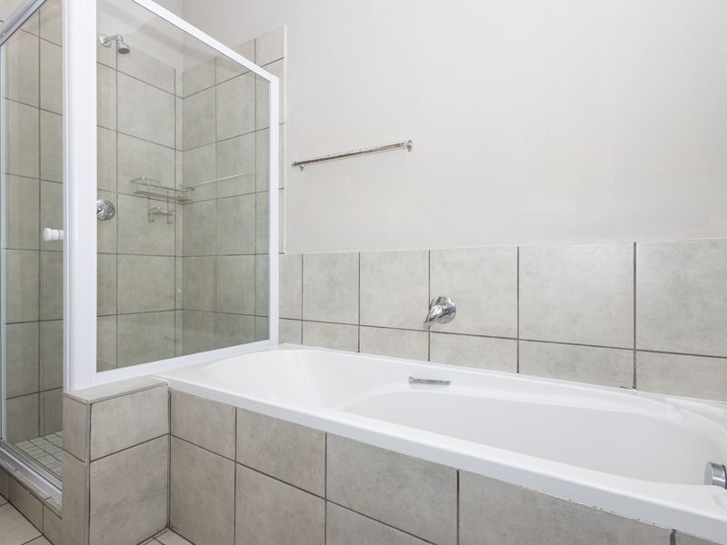 A clean, functional bathroom featuring a white bathtub, a separate glass-enclosed shower, and neutral ceramic wall tiling.