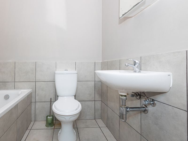 A functional bathroom featuring a wall-mounted basin, toilet, and bathtub with neutral ceramic tiling throughout.