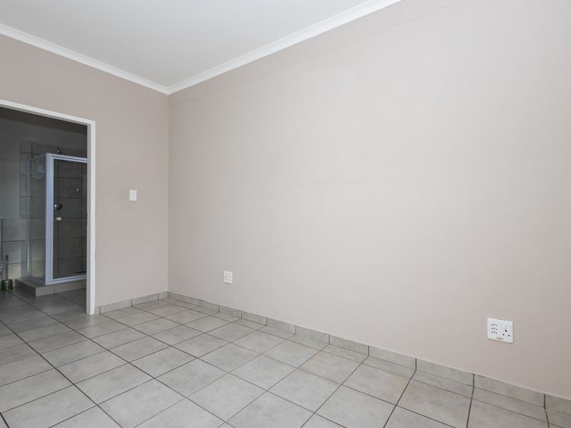 An empty bedroom featuring neutral wall paint, tiled flooring, and direct access to an en-suite bathroom.