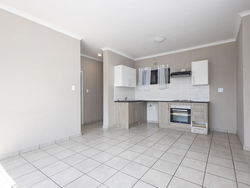 Open-plan kitchen and living area featuring tiled flooring, built-in cabinetry, and integrated cooking appliances in a neutral, well-lit space.