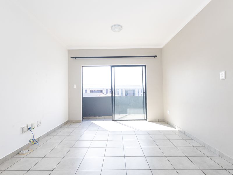 A bright, empty living room featuring neutral tiled flooring and a sliding glass door that opens onto a balcony.
