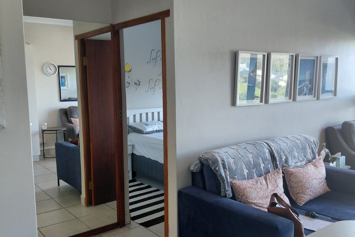 A living area featuring tiled flooring and a mirrored door leading to an adjacent bedroom, with neutral wall finishes and coved ceiling details.