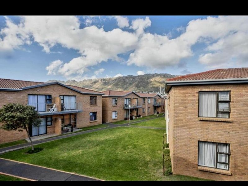 Exterior view of a residential apartment complex featuring face brick buildings, tiled roofs, balconies, and well-maintained communal garden areas with mountain views.