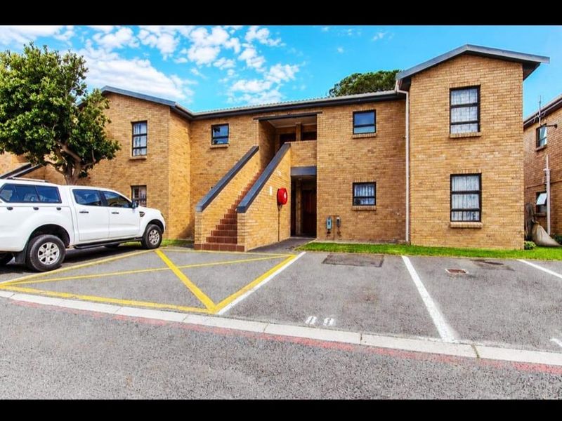 Exterior view of a face brick apartment building featuring an external staircase and dedicated asphalt parking bays.