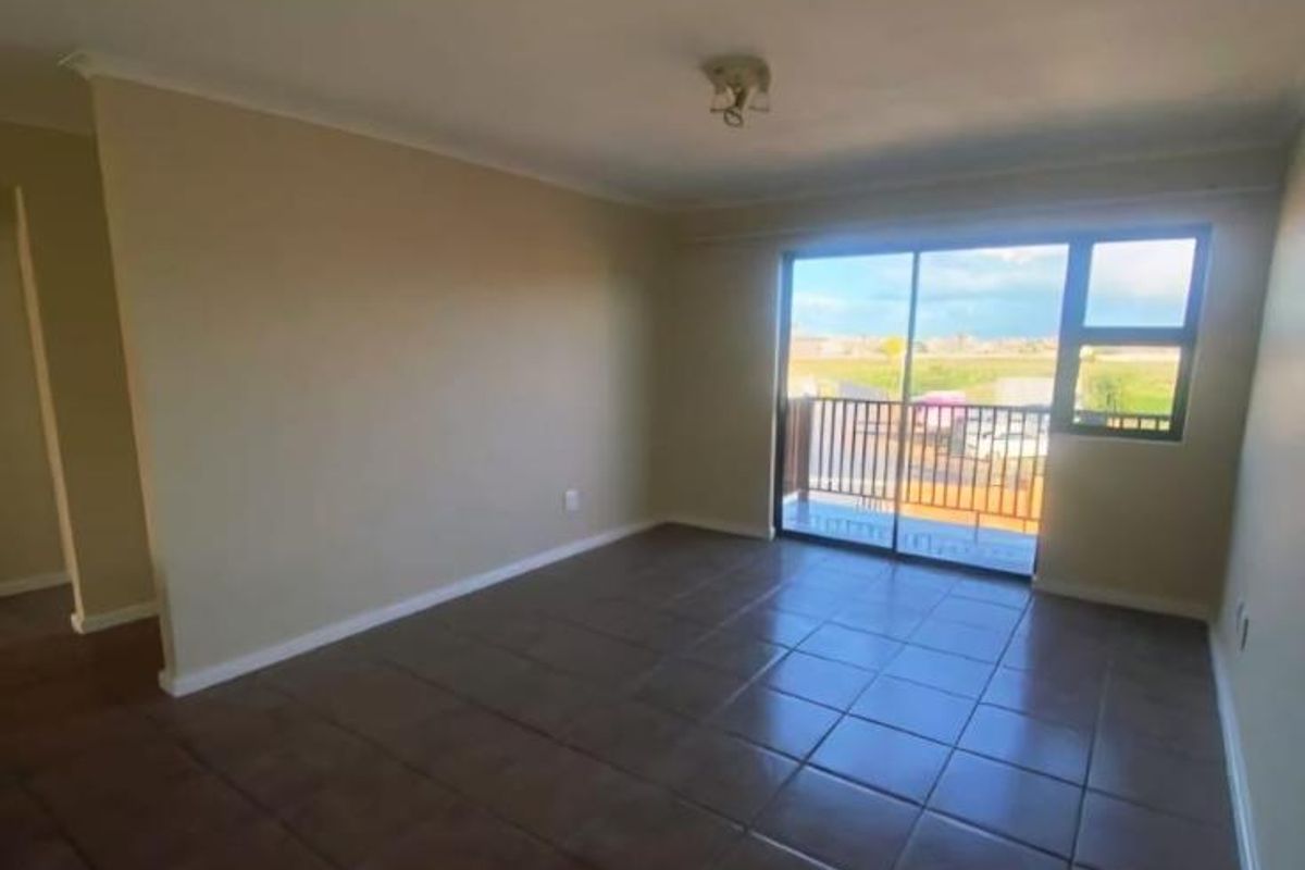An empty, neutrally painted living room featuring tiled flooring and a large sliding glass door providing access to a balcony.