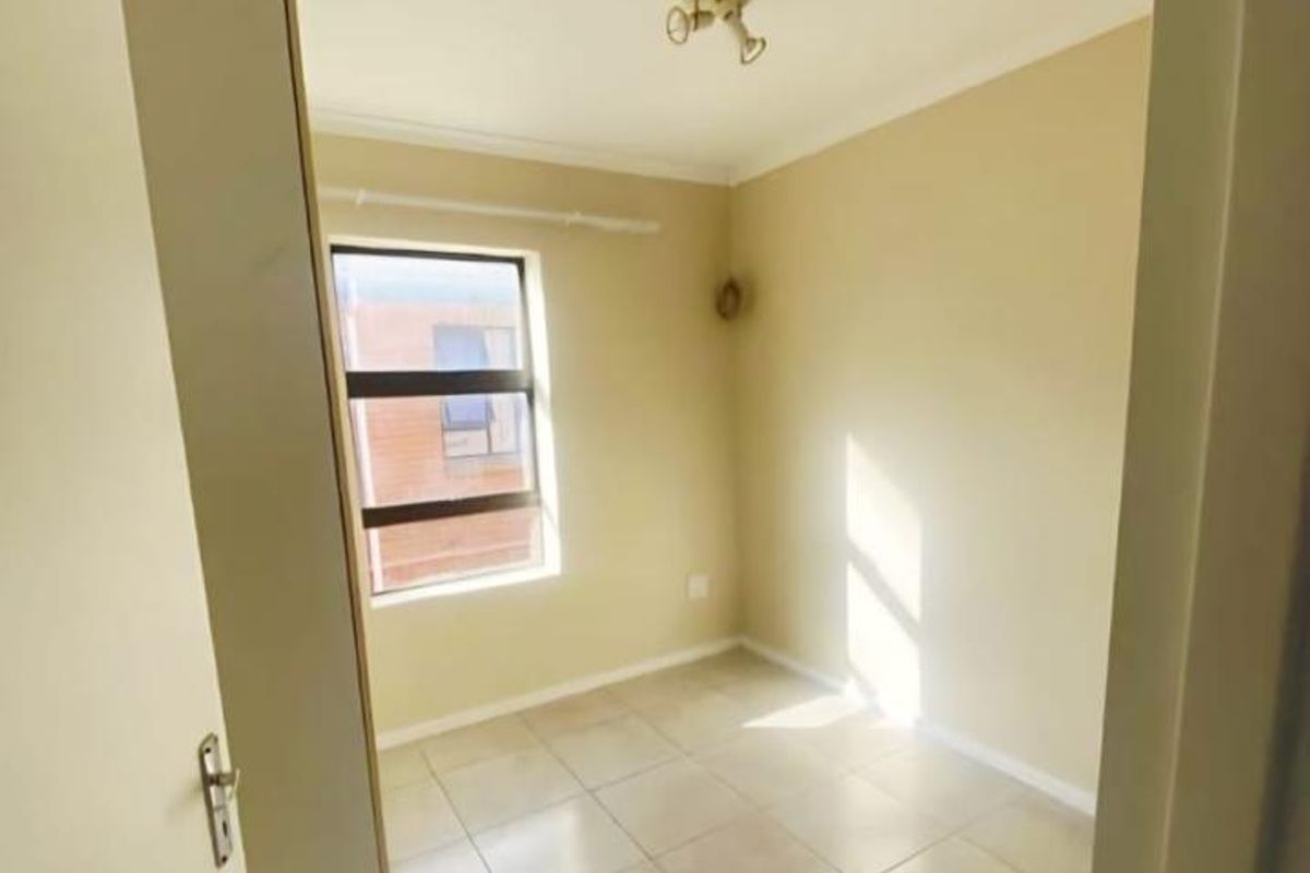 A bright, empty bedroom featuring neutral tiled flooring, a built-in cupboard, and an aluminium-framed window.