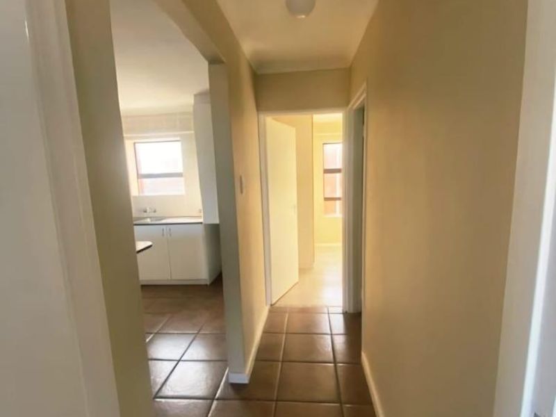 A clean, neutral-toned hallway featuring tiled flooring and access to adjacent rooms, including a view into the kitchen area.