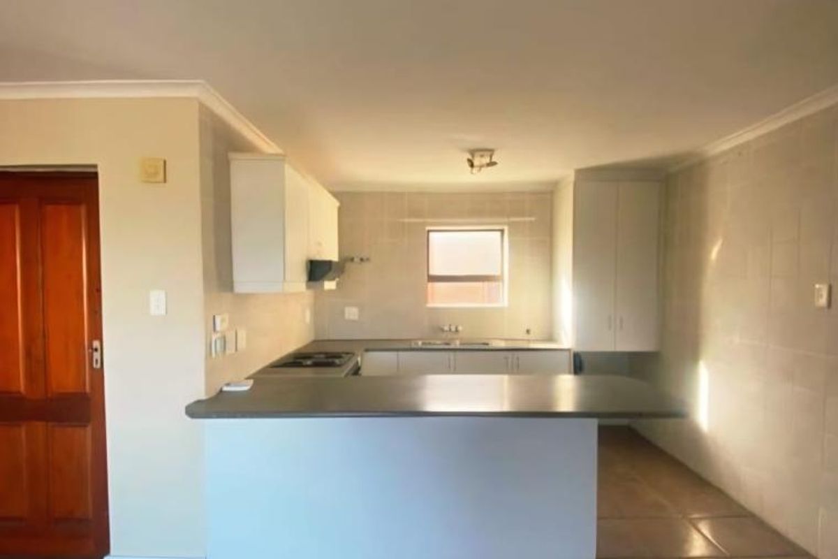 An empty kitchen featuring tiled flooring, built-in cabinetry, a central island, and a functional cooktop with an extractor fan.