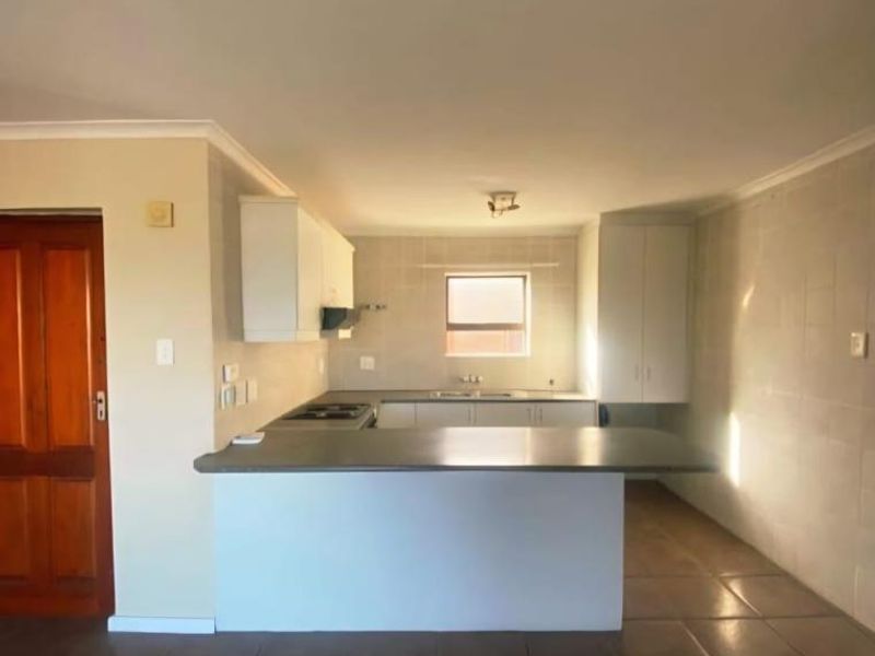 An empty kitchen featuring tiled flooring, built-in cabinetry, a central island, and a functional cooktop with an extractor fan.