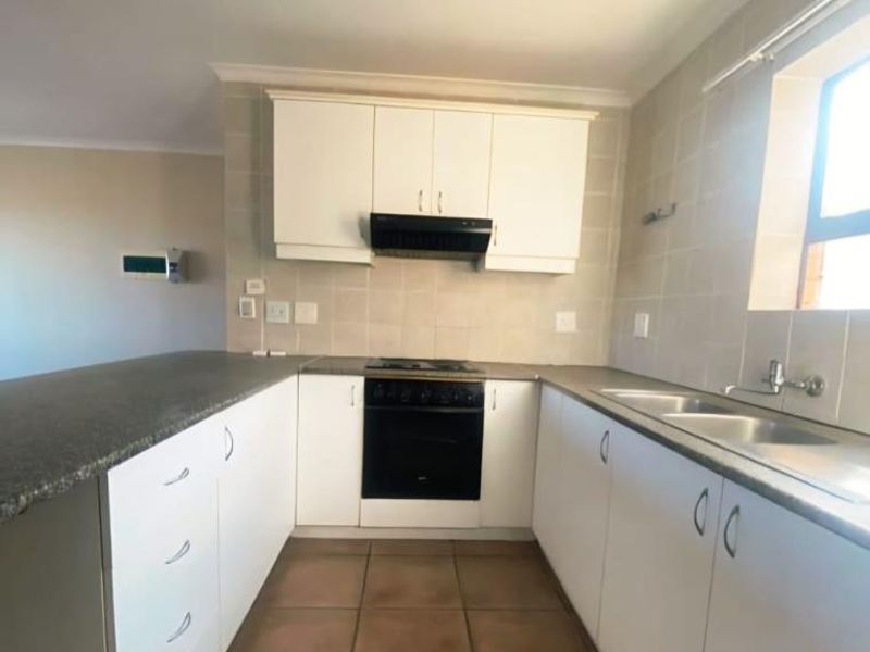 A functional kitchen featuring white built-in cabinetry, granite countertops, a double basin sink, and integrated cooking appliances with tiled flooring and splashbacks.