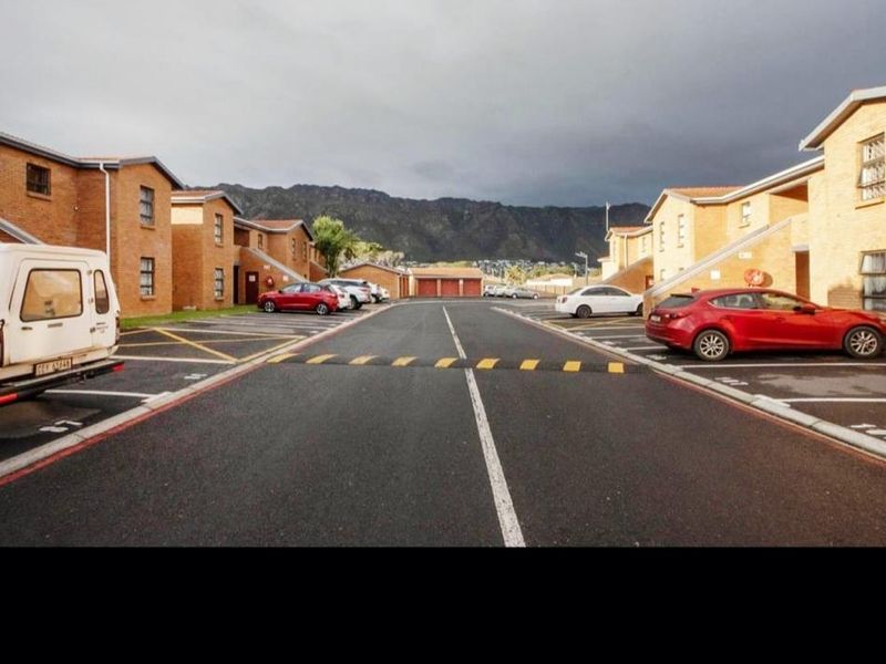 Exterior view of the apartment complex featuring a paved driveway, designated parking bays, and brick building facades with mountain views in the background.