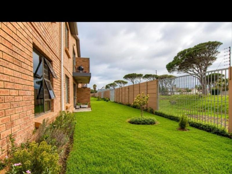 A well-maintained rear exterior view of the apartment building featuring a manicured lawn, face brick facade, and secure perimeter fencing.
