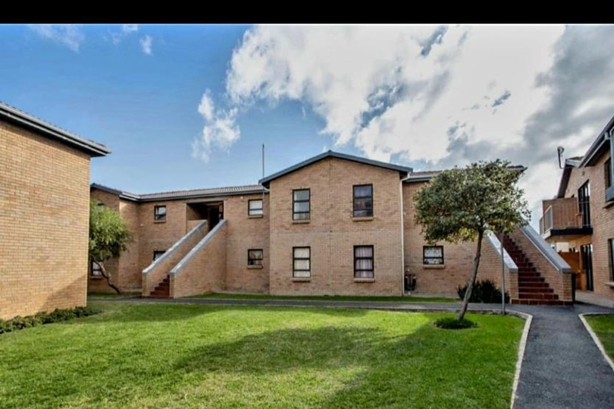 Exterior view of a multi-story brick apartment complex featuring communal lawn areas, paved walkways, and external staircases providing access to upper levels.