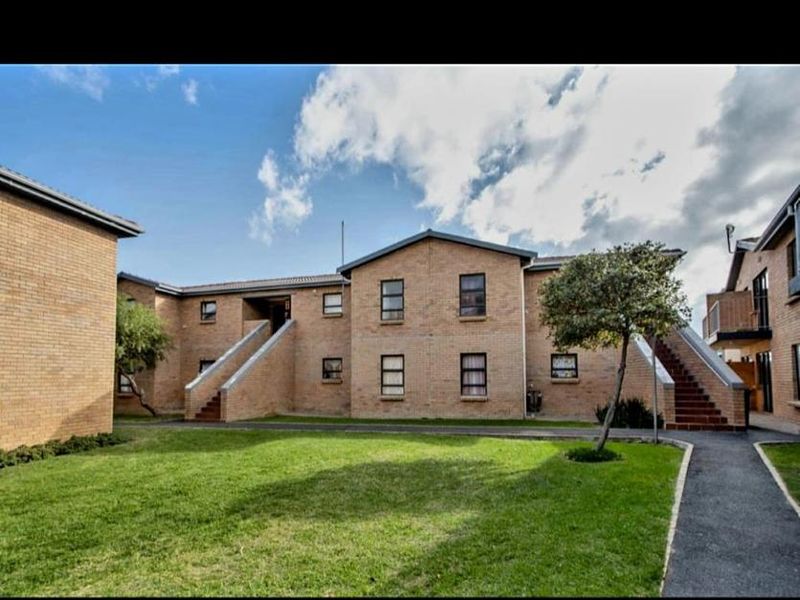 Exterior view of a multi-story brick apartment complex featuring communal lawn areas, paved walkways, and external staircases providing access to upper levels.