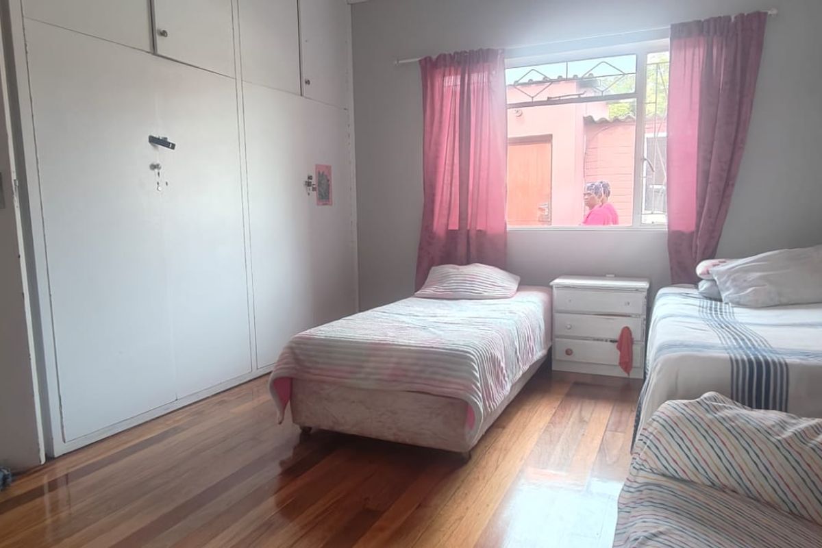 A bedroom featuring polished hardwood flooring and extensive built-in cupboard storage, providing a functional space with natural light.