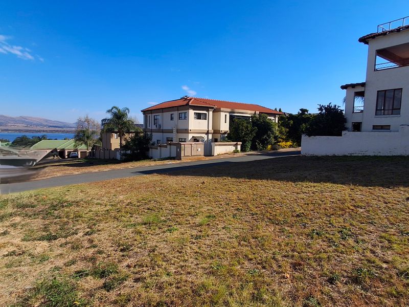 A vacant residential plot featuring a gentle slope, boundary wall, and views of the surrounding neighborhood and distant landscape.
