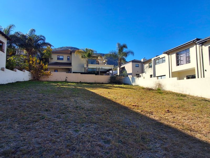 A vacant residential plot enclosed by boundary walls, situated in a developed neighborhood with surrounding multi-story residential properties.
