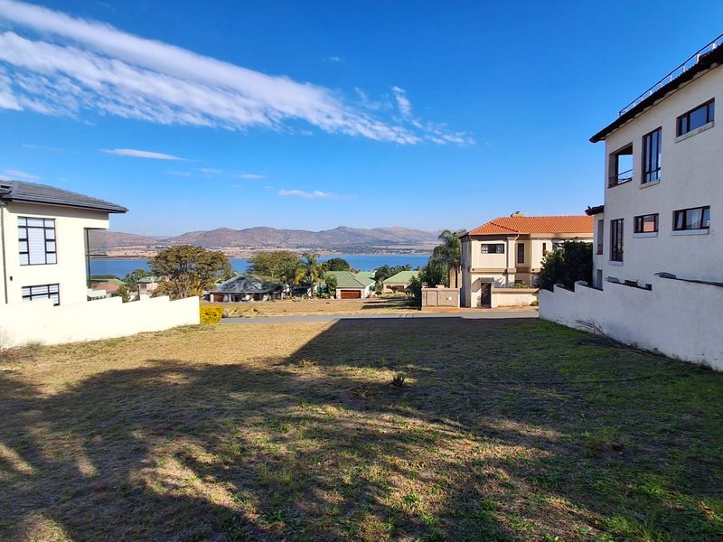A vacant residential plot situated between existing homes, offering clear views of the surrounding landscape and distant mountains.