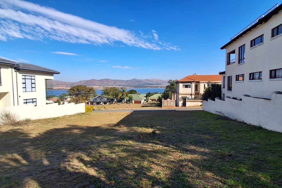 A vacant residential plot situated between existing homes, offering clear views of the surrounding landscape and distant mountains.