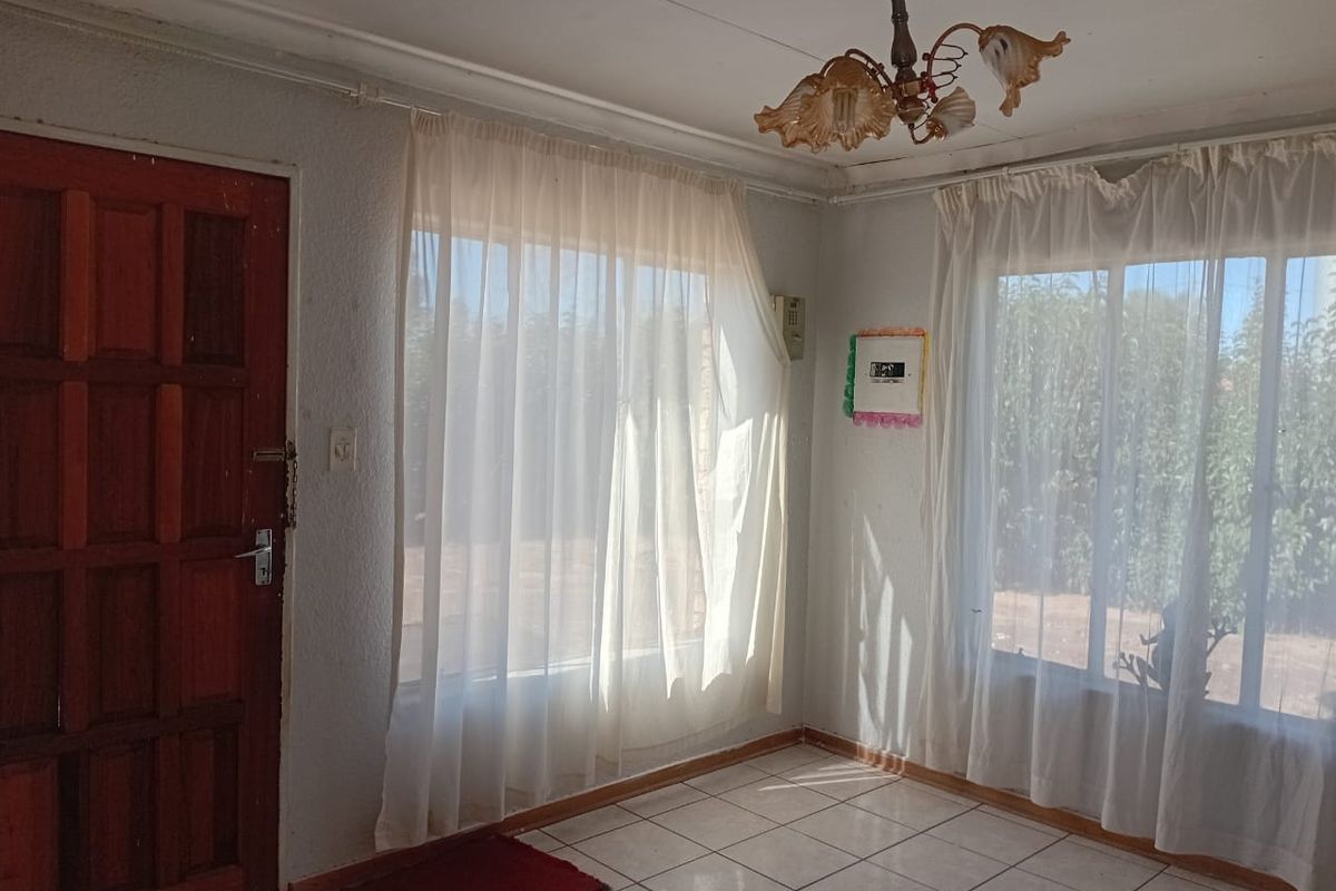 A bright, empty living area featuring tiled flooring, a timber entrance door, and large windows allowing for ample natural light.