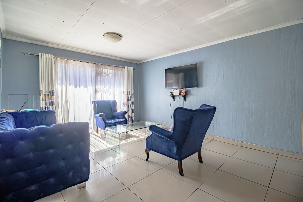 A living room featuring tiled flooring and a sliding glass door with security gate, providing access to the exterior.