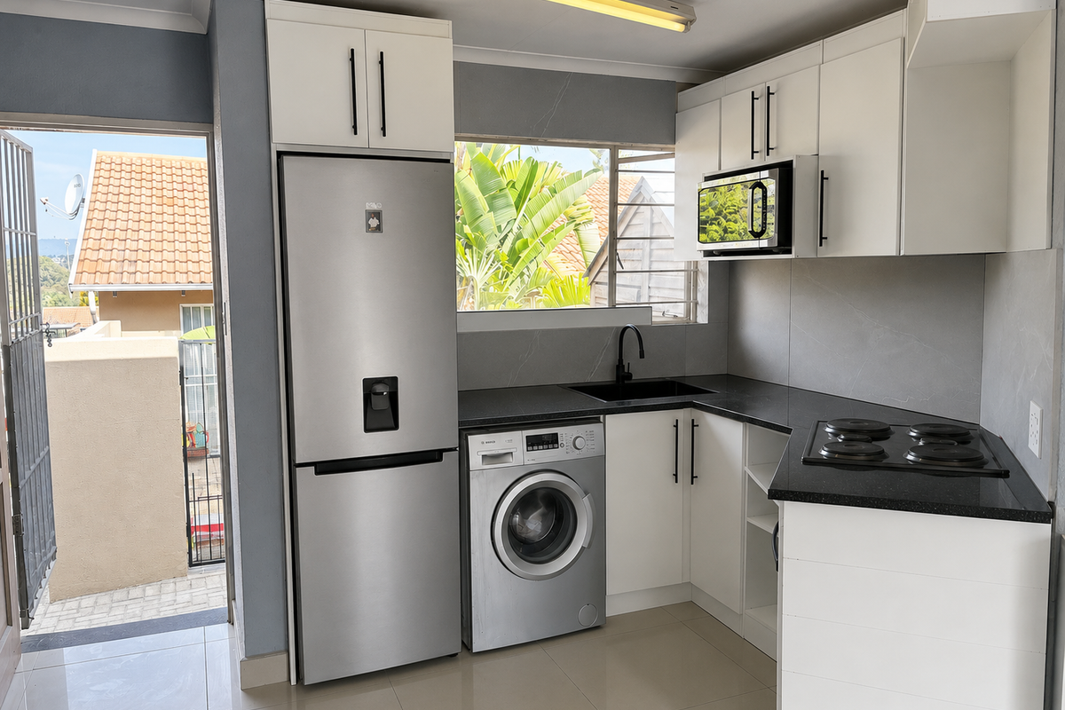 Modern kitchen featuring white cabinetry, black stone countertops, integrated appliances, and a black sink, with direct access to an outdoor patio area.
