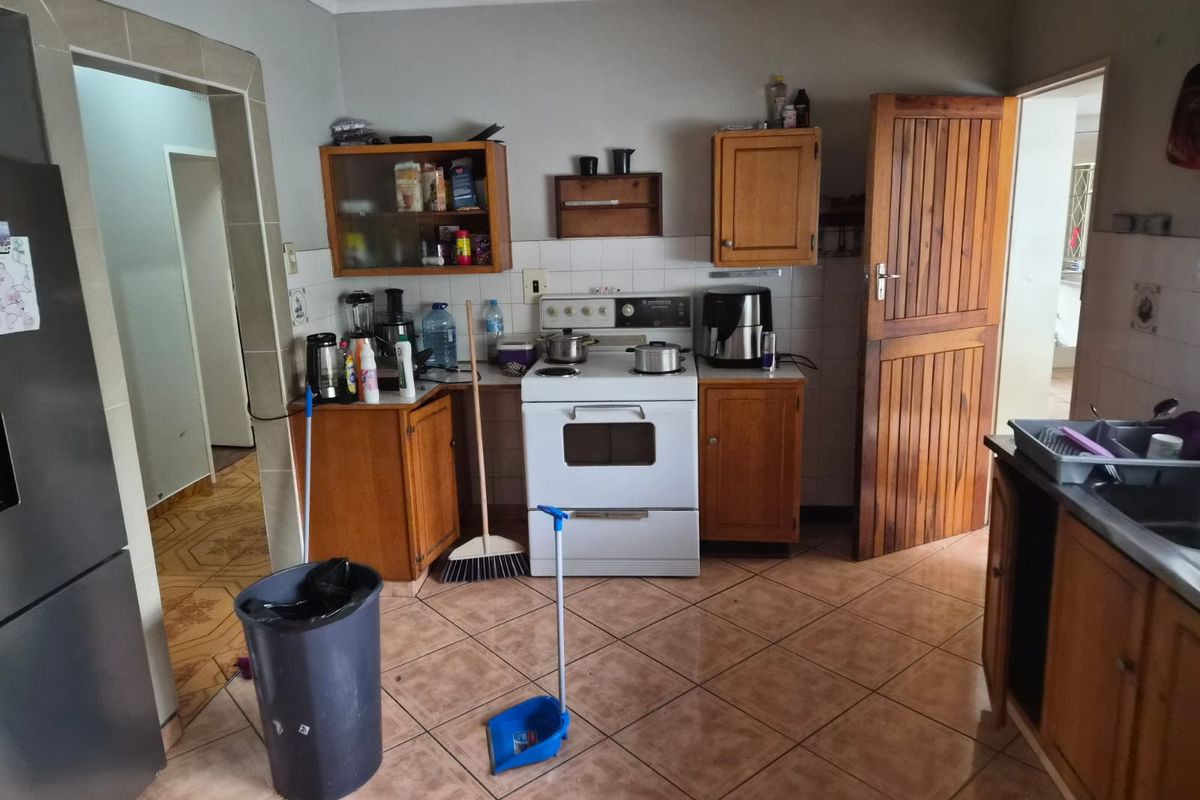 A functional kitchen featuring wooden cabinetry, tiled flooring, and a freestanding stove, offering a practical layout with direct access to adjacent rooms.