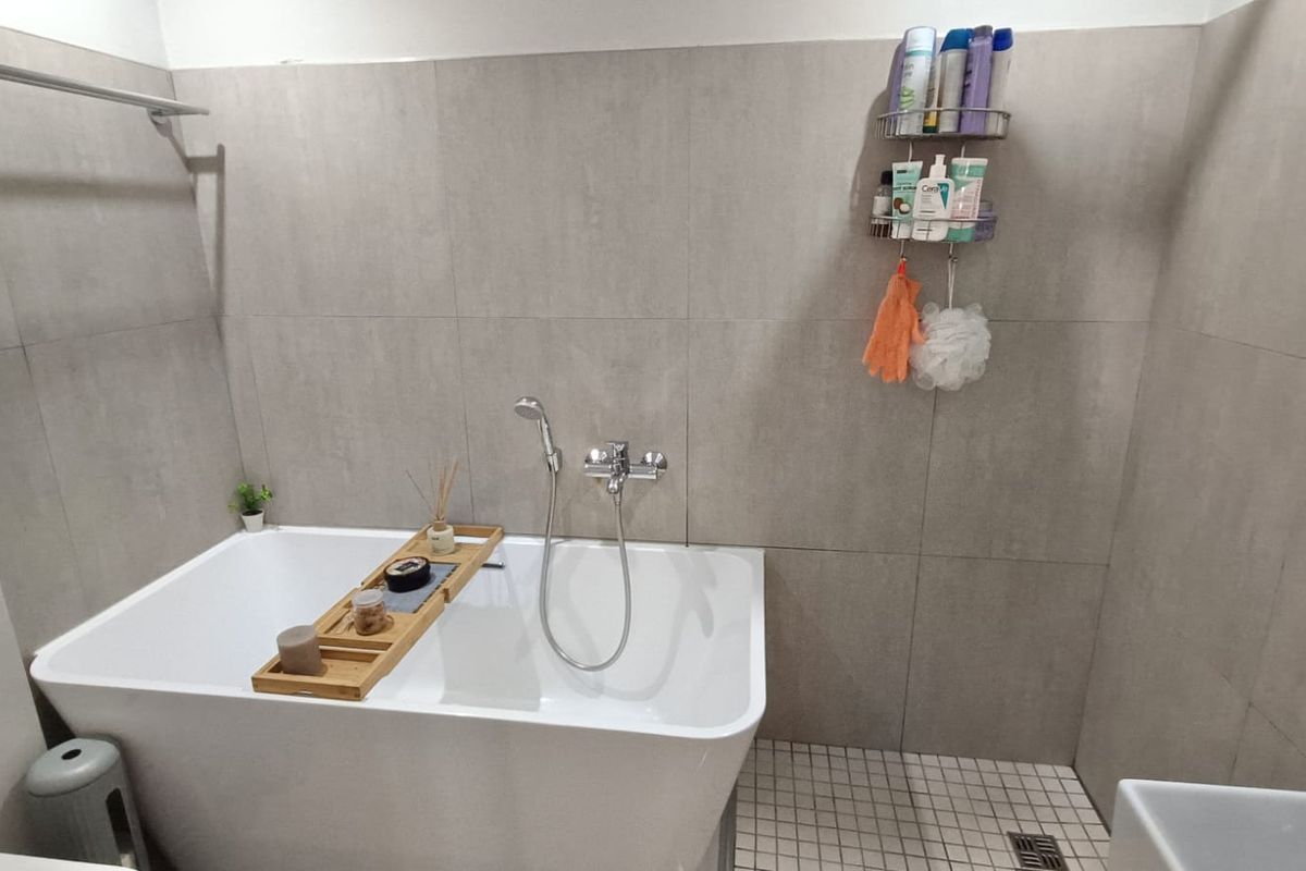 Modern bathroom featuring a sleek freestanding bathtub with wall-mounted shower mixer and neutral large-format wall tiling.