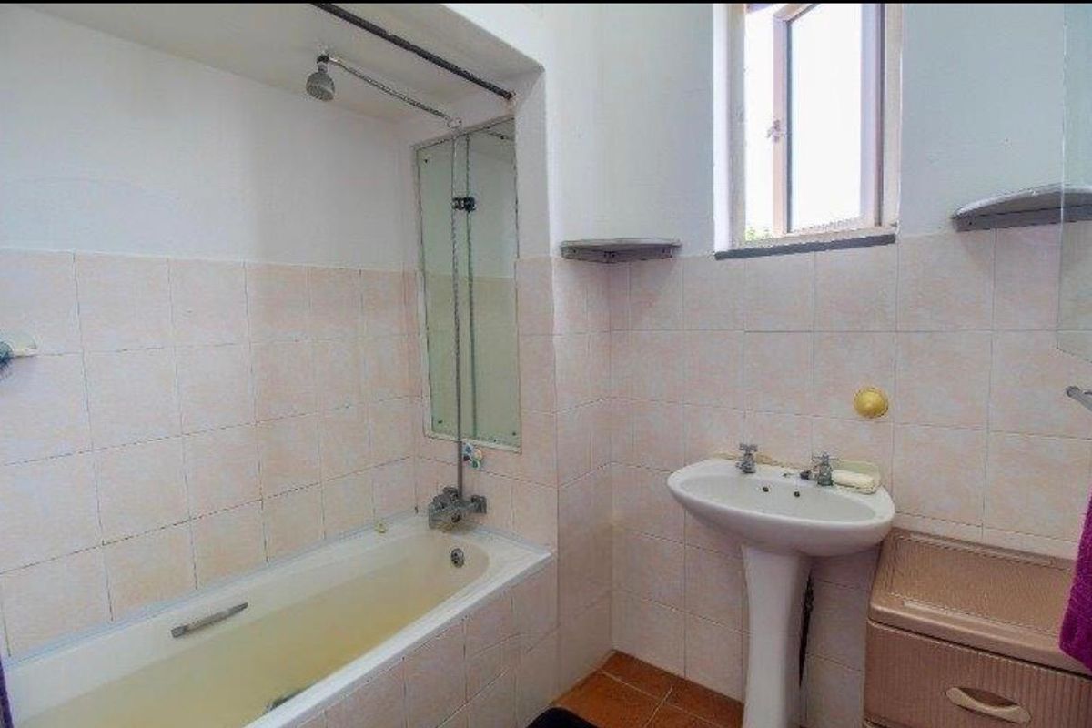 A dated bathroom featuring a pedestal basin, built-in bathtub with shower head, and tiled wall finishes.