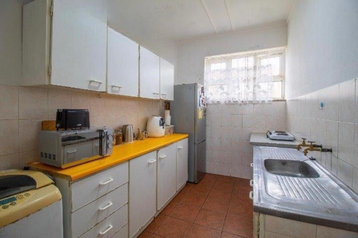 A functional kitchen featuring white cabinetry, a yellow laminate countertop, stainless steel sink, and tiled flooring, offering potential for modernization.