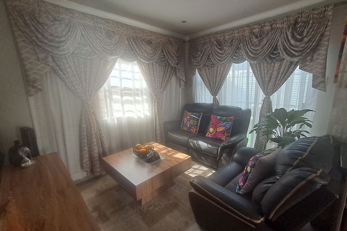 A cozy living room featuring coved cornicing and recessed downlighting, with large windows dressed in decorative drapery.