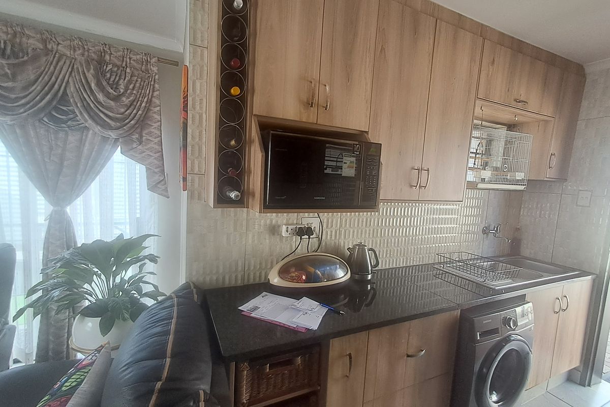 Compact kitchen featuring light wood-finish cabinetry, dark countertops, tiled backsplash, and integrated appliances including a washing machine and microwave.