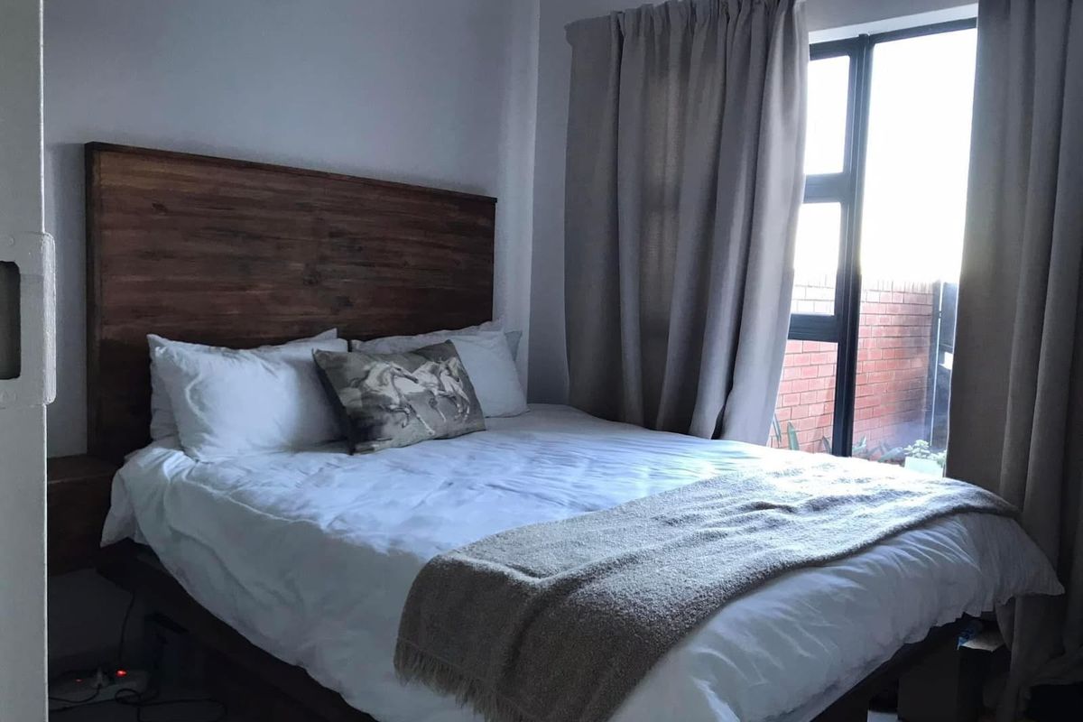 A well-lit bedroom featuring a large window with curtains and a built-in wooden headboard.