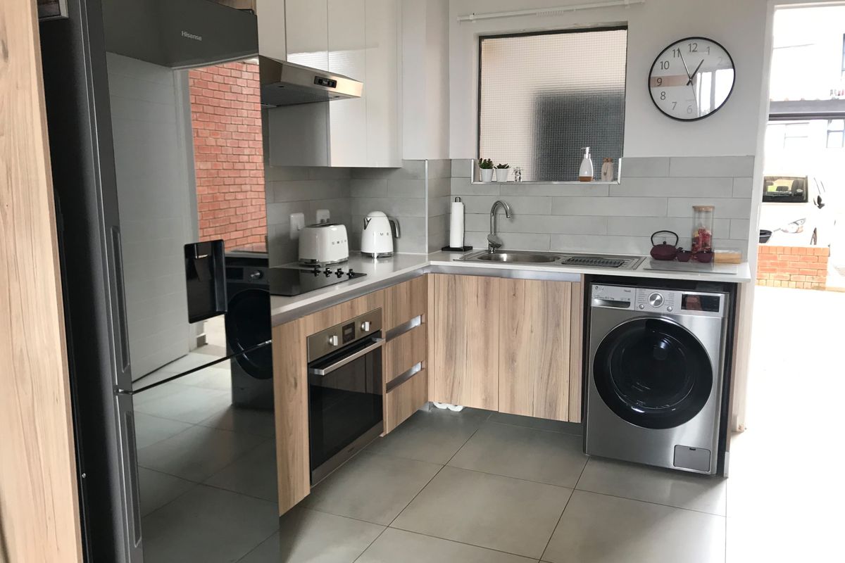 Modern kitchen featuring light wood-grain cabinetry, stone-look countertops, integrated stainless steel oven, hob, extractor fan, and dedicated space for laundry appliances.