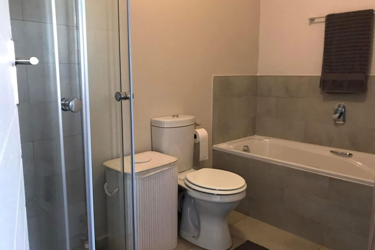 A functional bathroom featuring a glass-enclosed shower, a built-in bathtub with tiled surround, and a standard toilet.