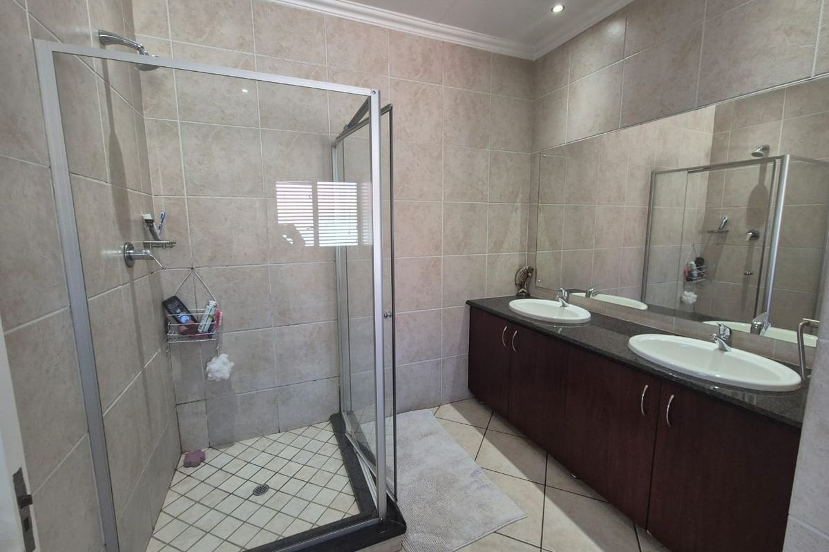 A well-maintained bathroom featuring a glass-enclosed shower, a double vanity with granite countertops, and large wall-mounted mirrors.
